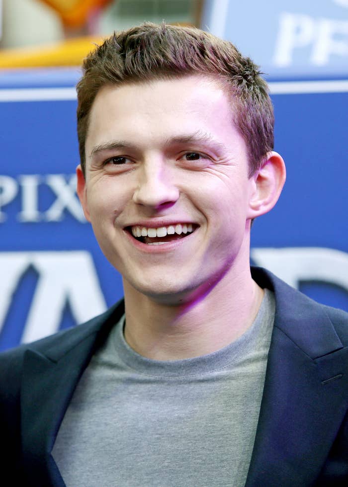 Tom Holland, in a blazer and T-shirt, smiling widely