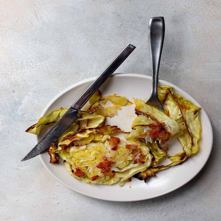 A roasted cabbage steak on a plate with bacon.