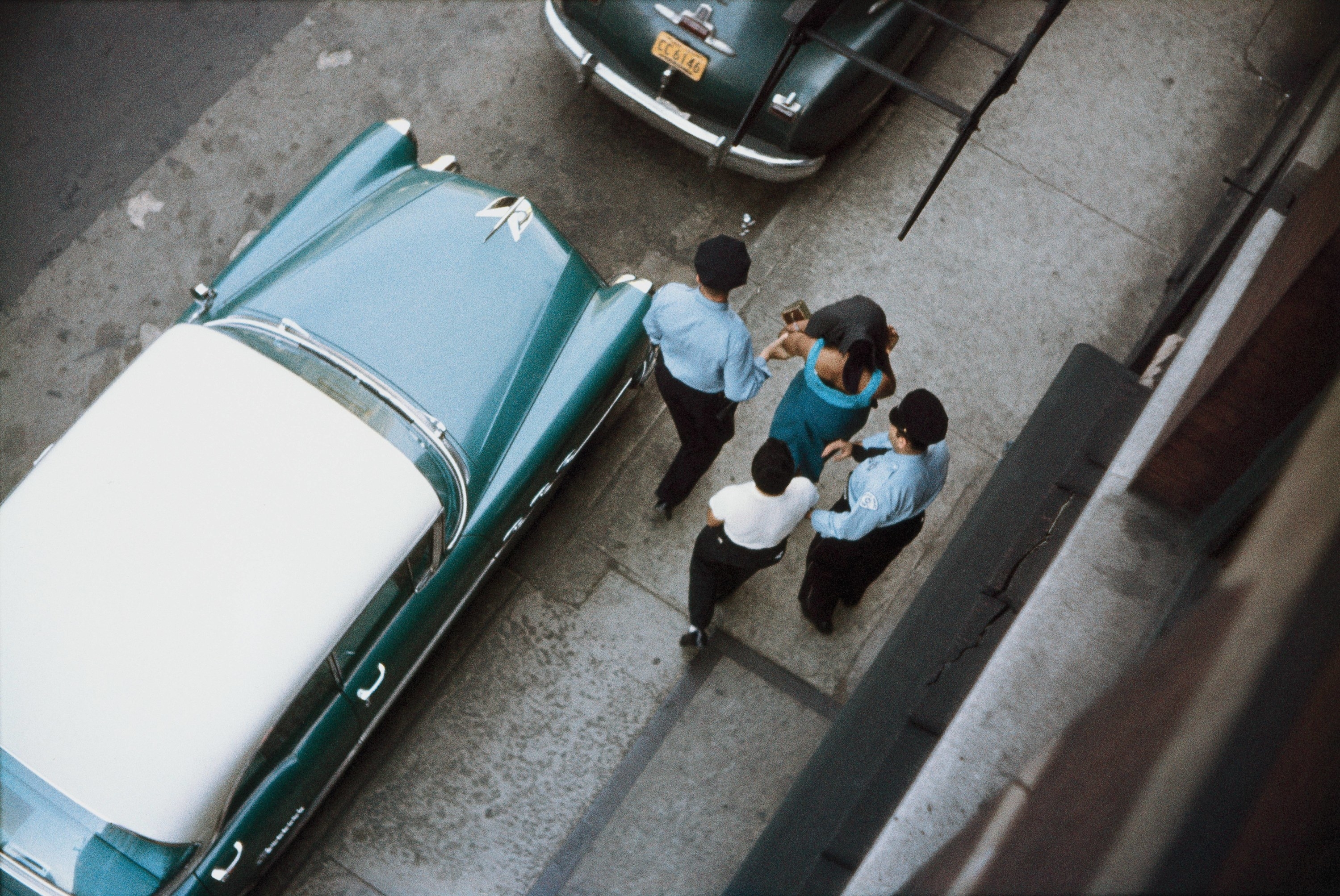 An overhead shot of two policemen leading away a woman down a street with a man behind her