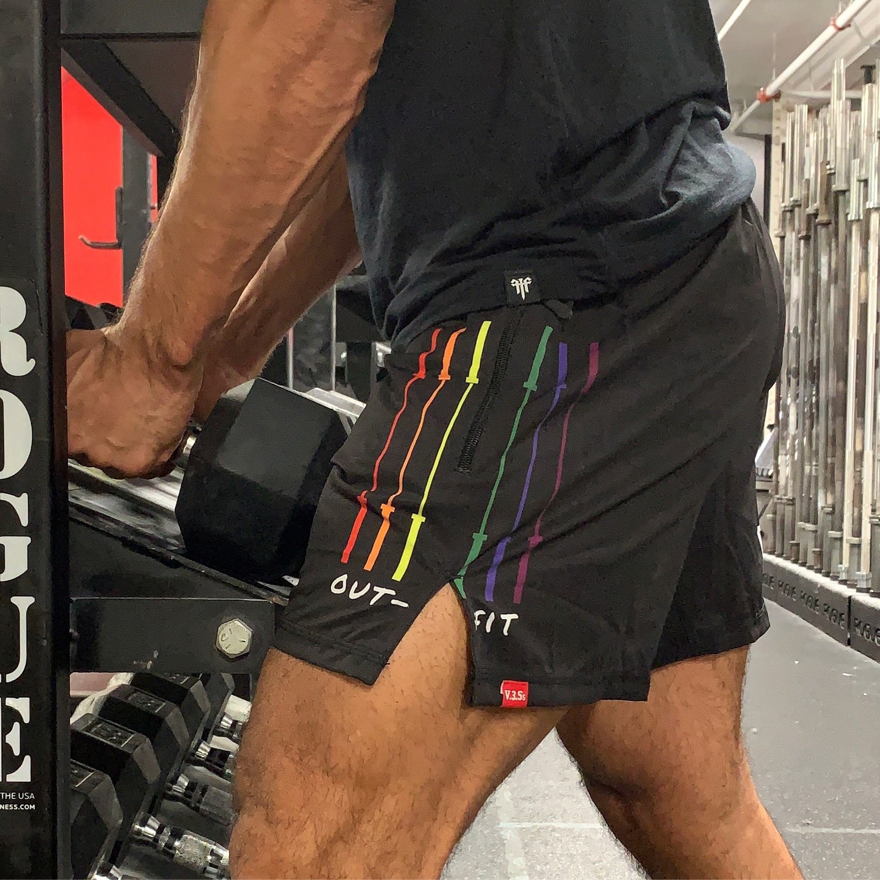 a model wearing the shorts with a rainbow logo on the bottom next to barbells