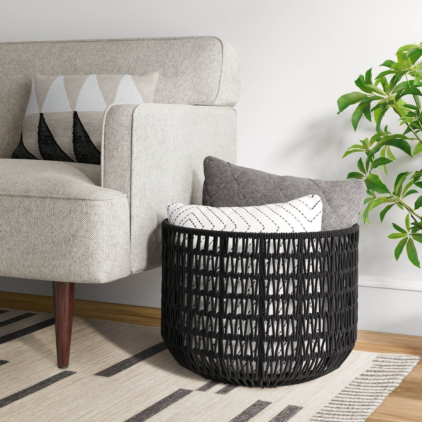 the woven rope basket in black sitting next to a couch with pillows in it