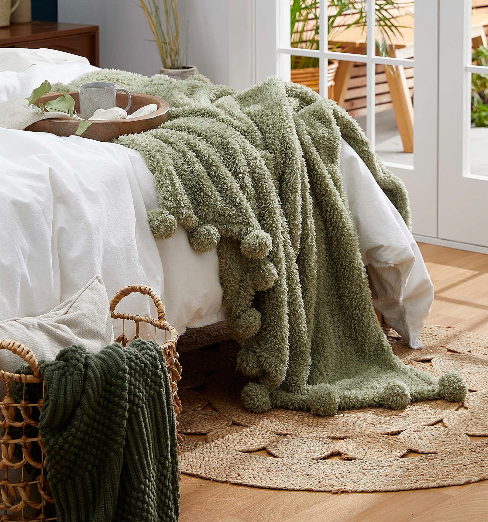 A soft blanket with a pom pom trim on the edge of a bed