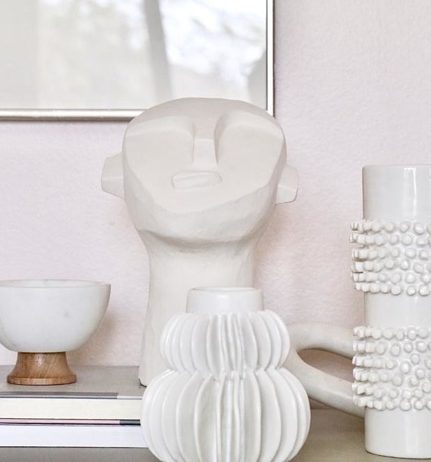 the small white statue that looks like a face with a long neck sitting on a table