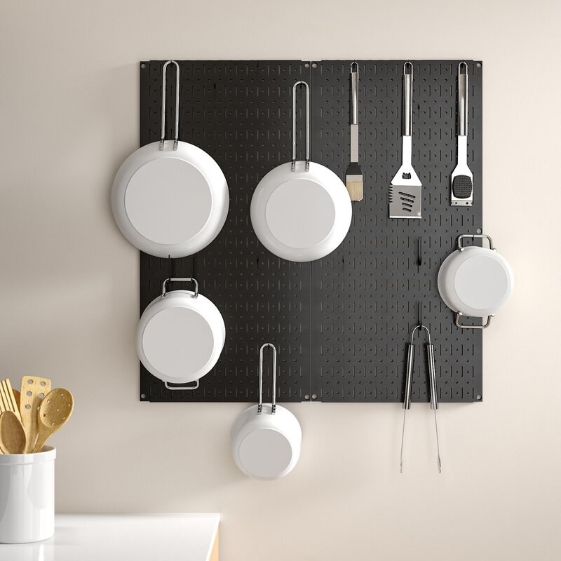 the black rectangle pegboard with assorted pots, pans, and utensils hanging off of it
