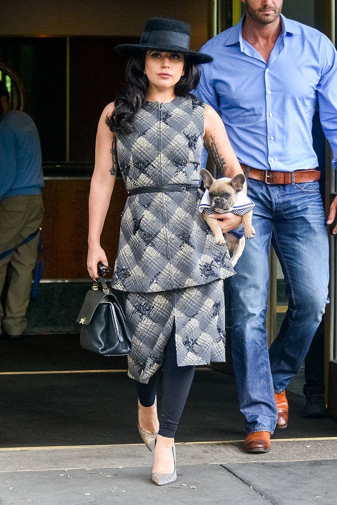 Lady Gaga walking out of a building while carrying one of her dogs