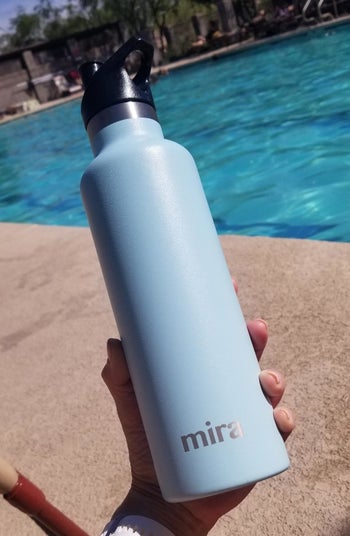 reviewer holding the water bottle in blue by a pool