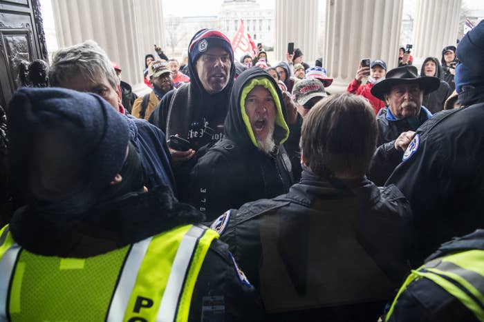 An unmasked man in a hooded jacket screams at a line of police officers wearing hi-vis vests