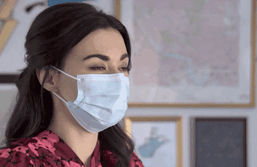 A woman puts on a patterned face mask over a medical face mask