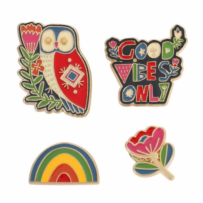 4 enamel pins - Top, from left: A colourful owl next to a flower and a good vibes only pin in the style of typography. Bottom, from left: A rainbow pin with 5 colours and a flower pin.