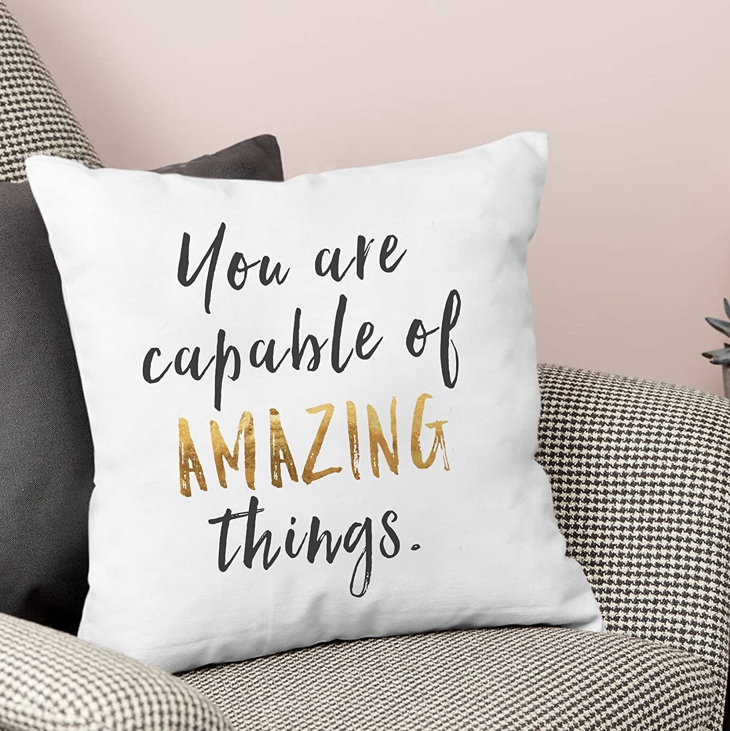 A white cushion cover with the words, &quot;You&#x27;re capable of amazing things.&quot; in black and gold.