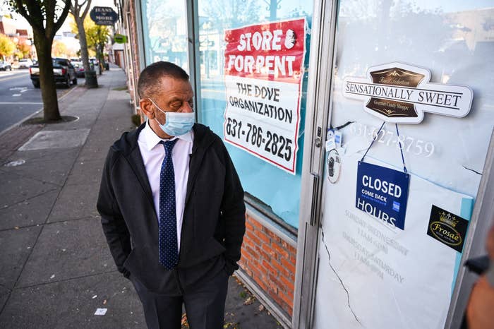 Man wearing a mask stands outside a shuttered business