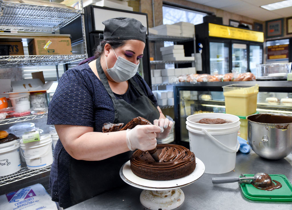 Masked worker frosting a cake in a restaurant kitchen