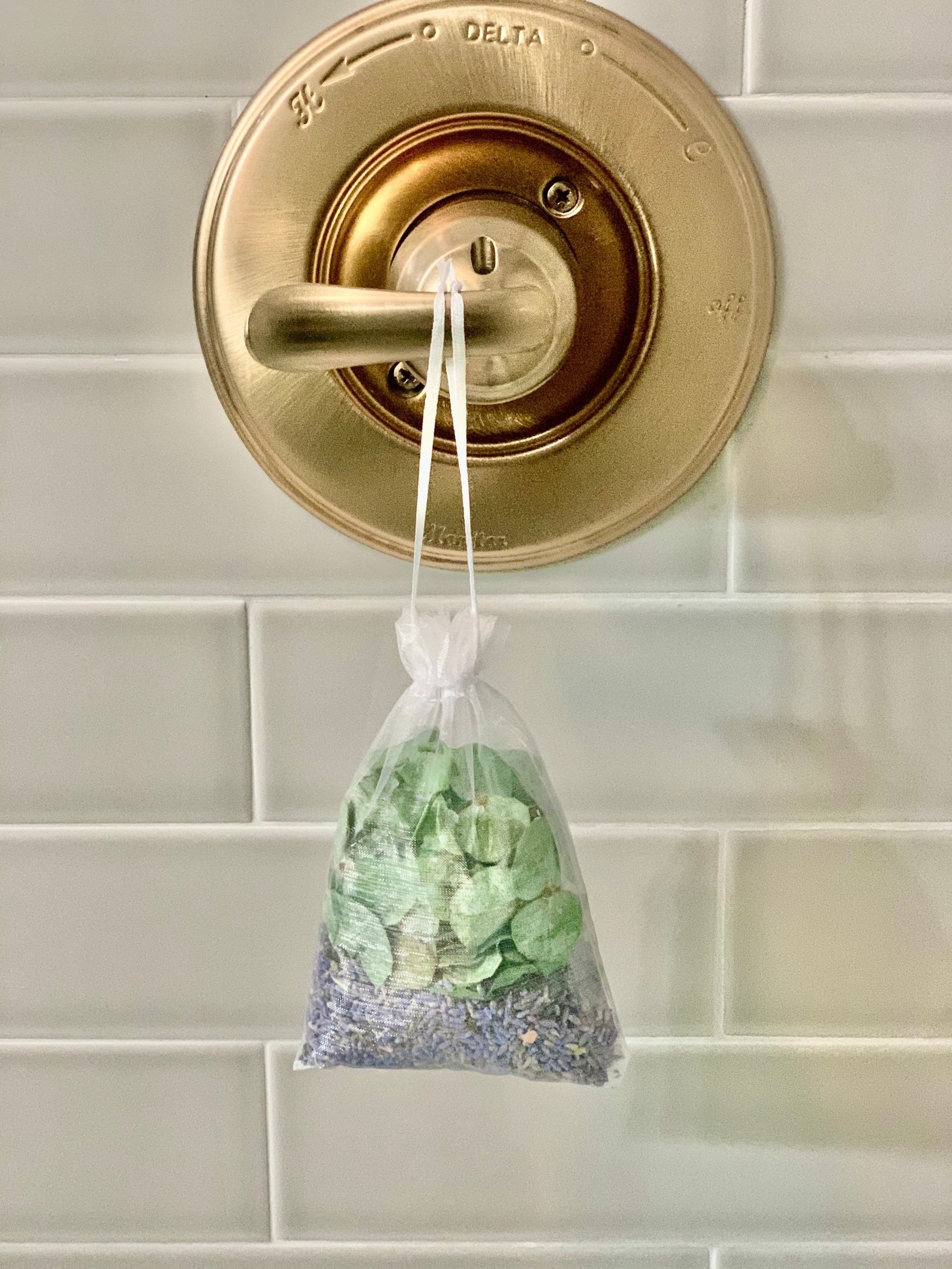 A small satchel of lavender and eucalyptus hanging from a bath handle 