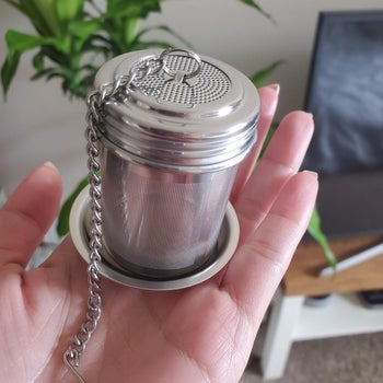 A reviewer photo of a hand holding out the mesh tea strainer on the included saucer