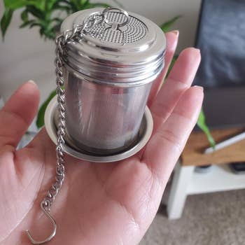A reviewer photo of a hand holding out the mesh tea strainer on the included saucer 