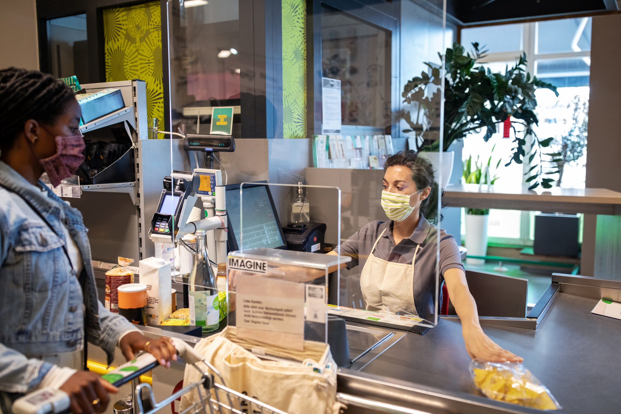 A grocery store employee working during COVID, standing behind a plastic wall while wearing a mask