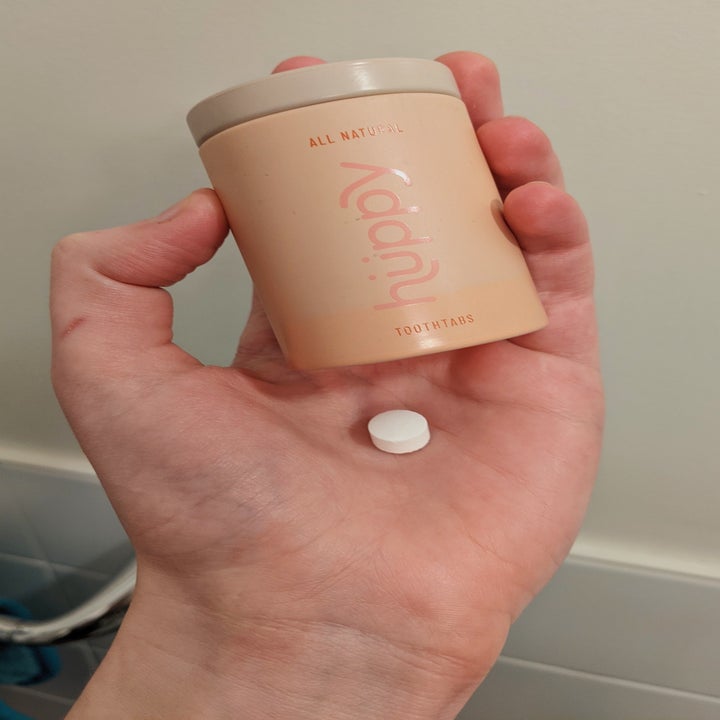 A hand holding a pink tin and a white tab 