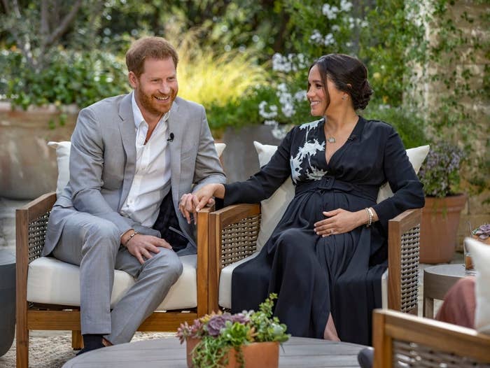 Harry and Meghan sitting on two chairs while holding hands