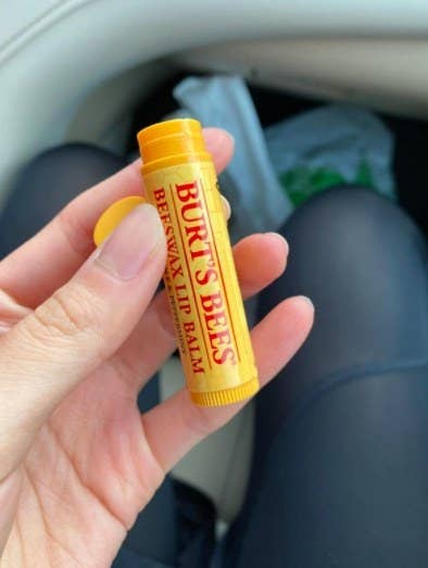 person holding up a burt's bees beeswax lip balm to the camera