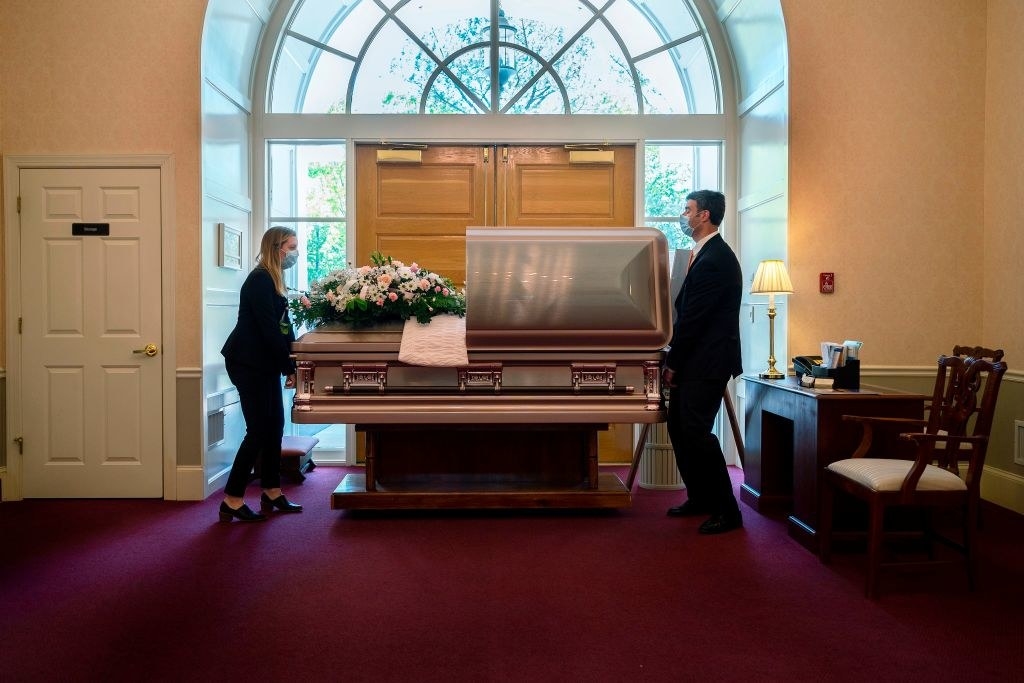 Two people carrying a casket in a funeral home while wearing masks