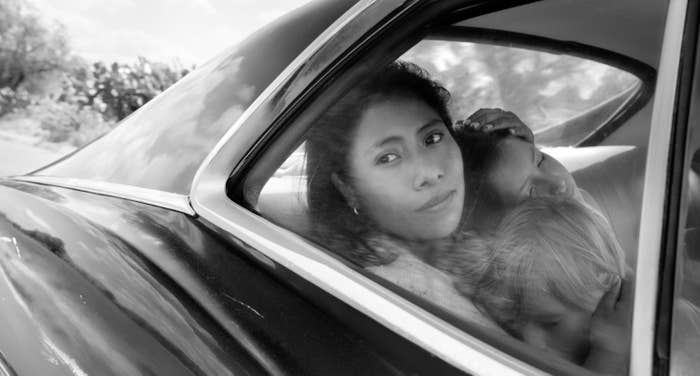 Yalitza as Cleo sitting in a moving car and holding two children in her arms in a scene from Roma