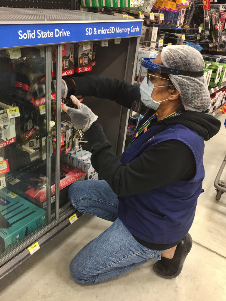 A Walmart employee wearing a face mask and face shield while stocking items in a cabinet