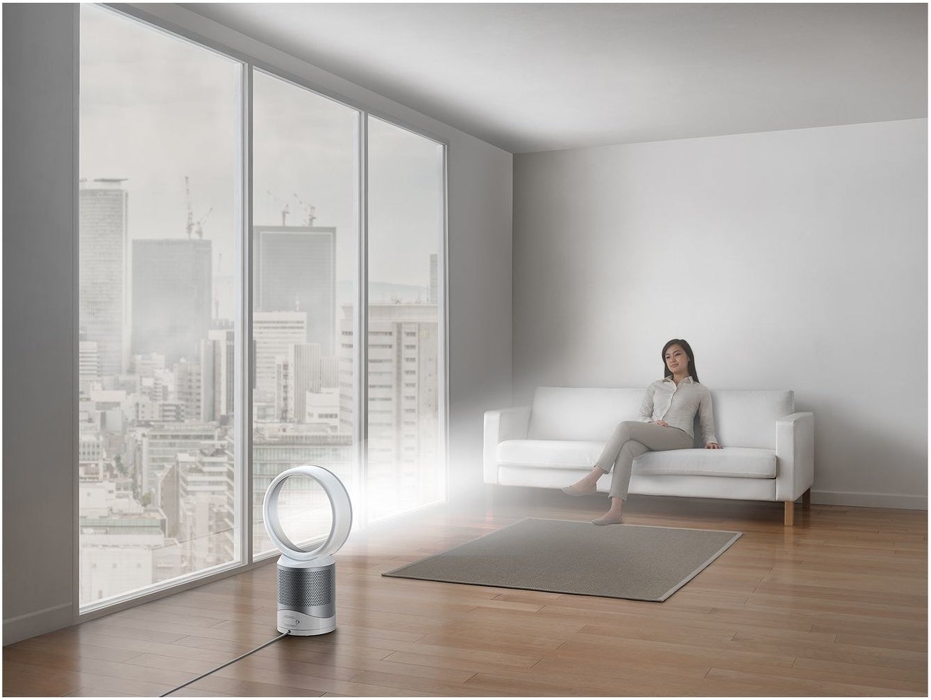 woman sitting on a couch next to a Dyson air purifier and fan in a living room