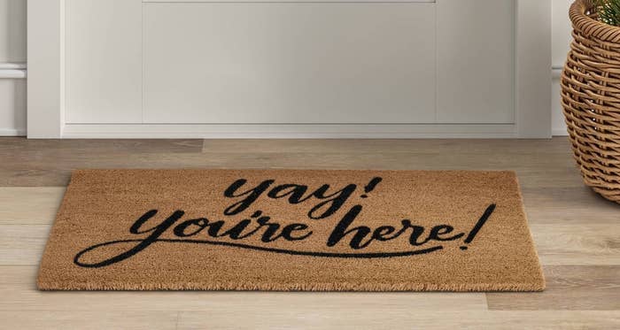 Tan welcome mat with black typography and design