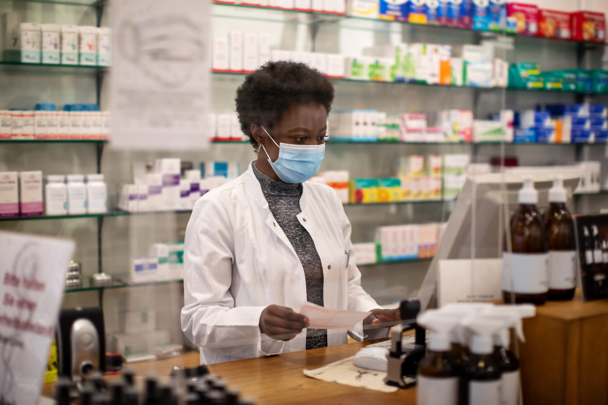 Pharmacist working during COVID - wearing a mask while working behind a plastic protected shield