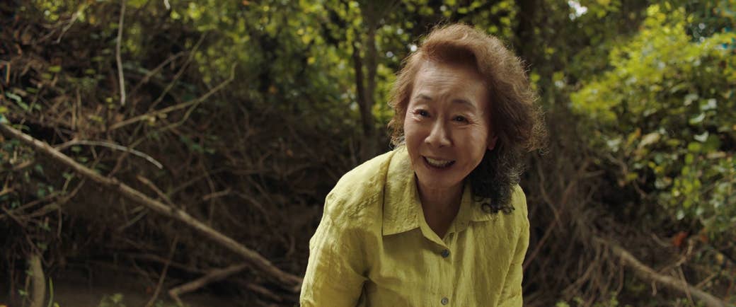 An older woman in a yellow shirt in front of plants outdoors in a still from Minari