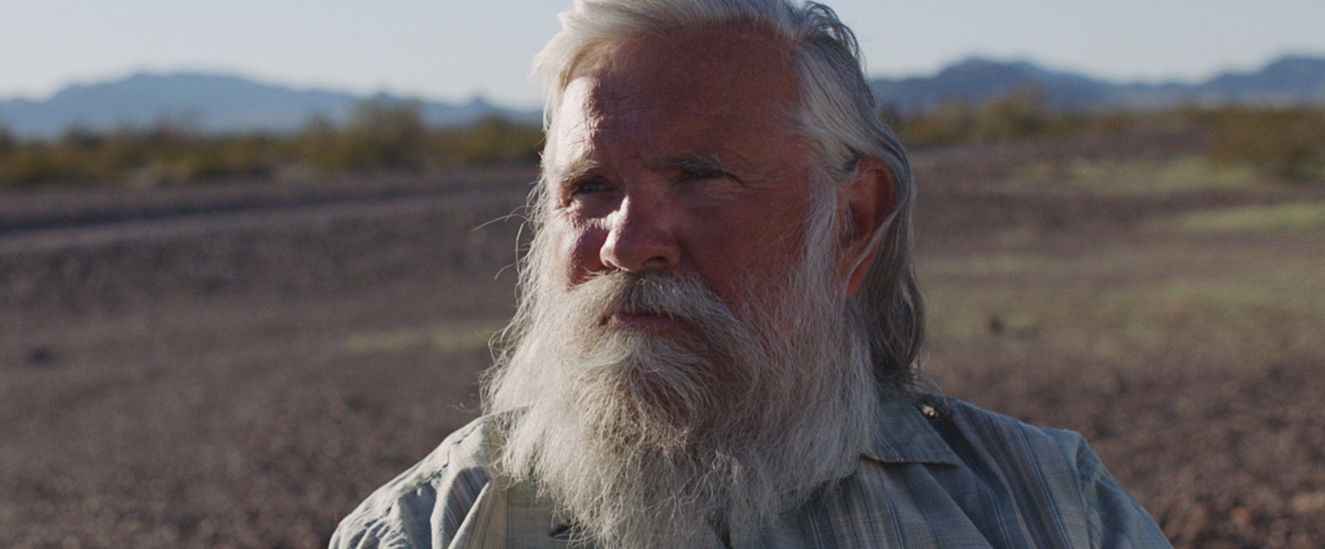 An older man with a beard in front of a desert background