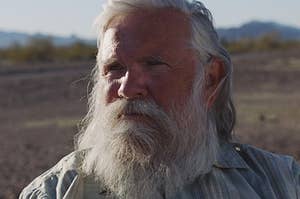 An older man with a beard in front of a desert background. 