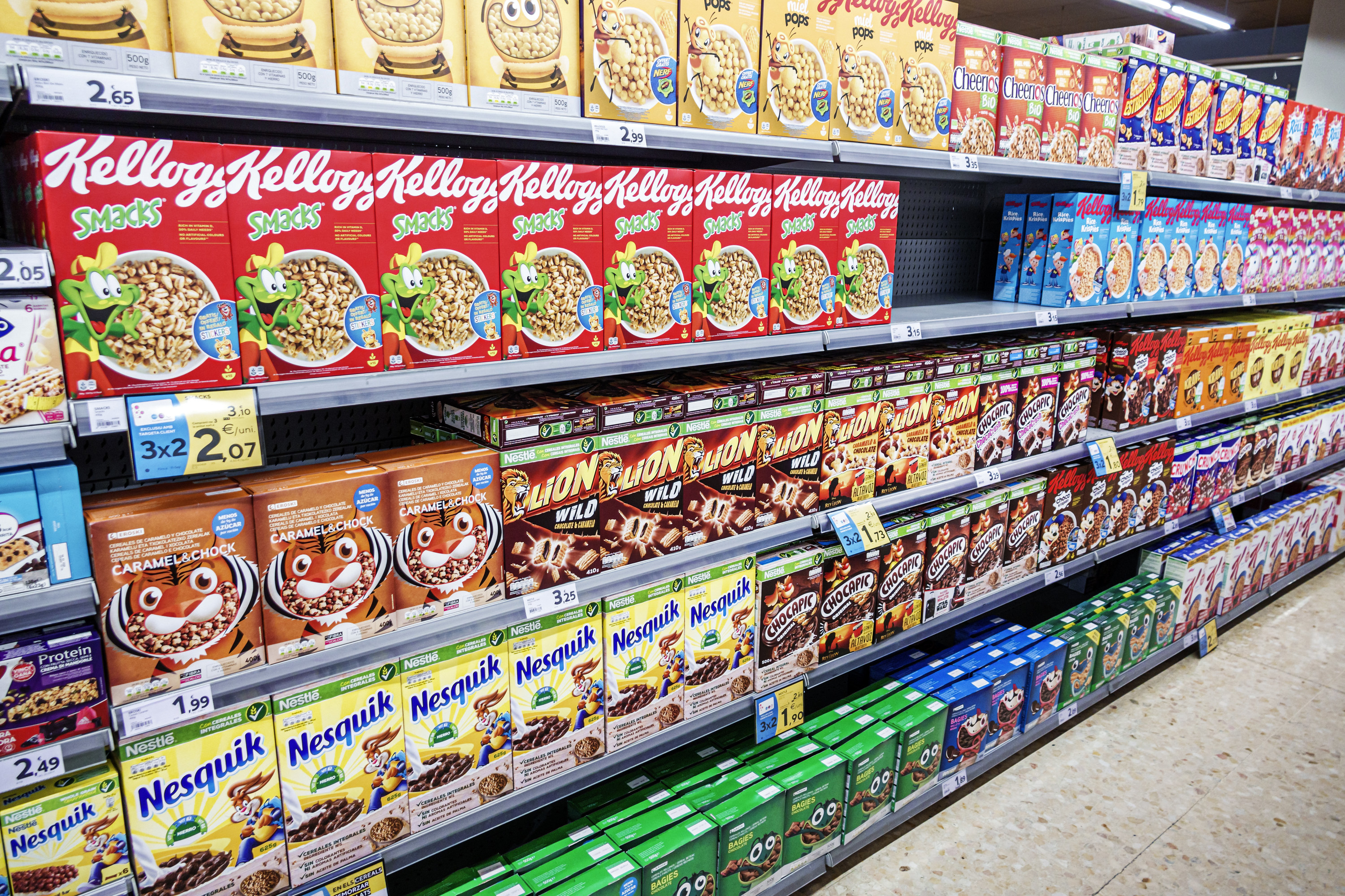 Grocery store aisle with multiple shelves stocked with different colorful cereal boxes