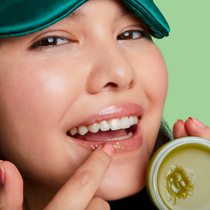 A smiling person applying the green tea mask to their lips