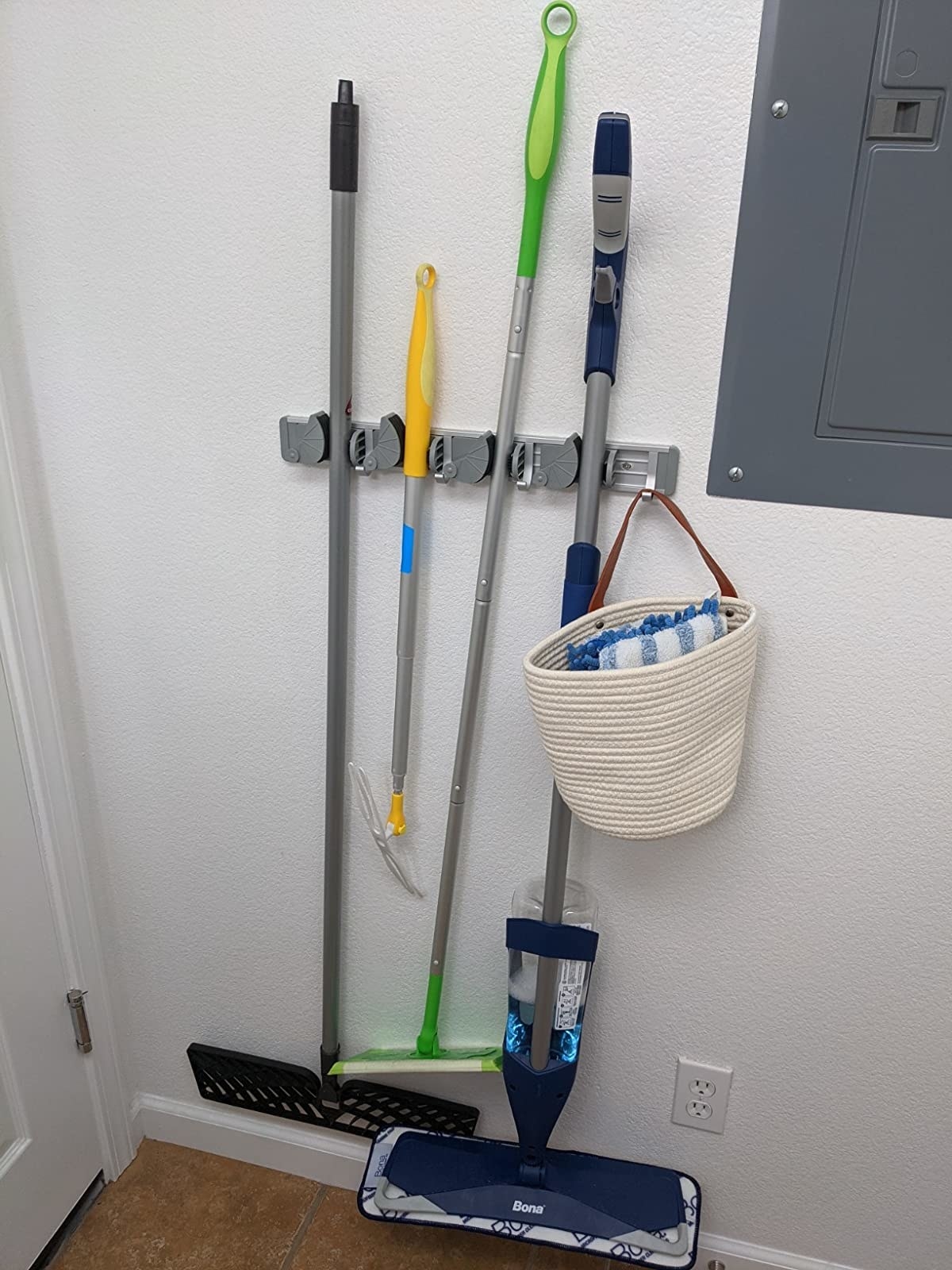 The rack, which holds mops, rooms, and even bags from a series of small, adjustable hooks