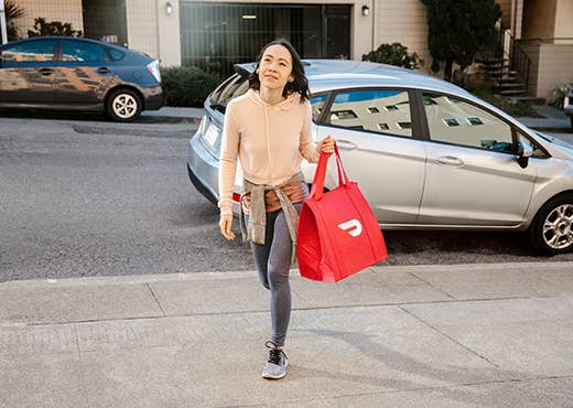 Woman walks away from car holding a DoorDash delivery. 