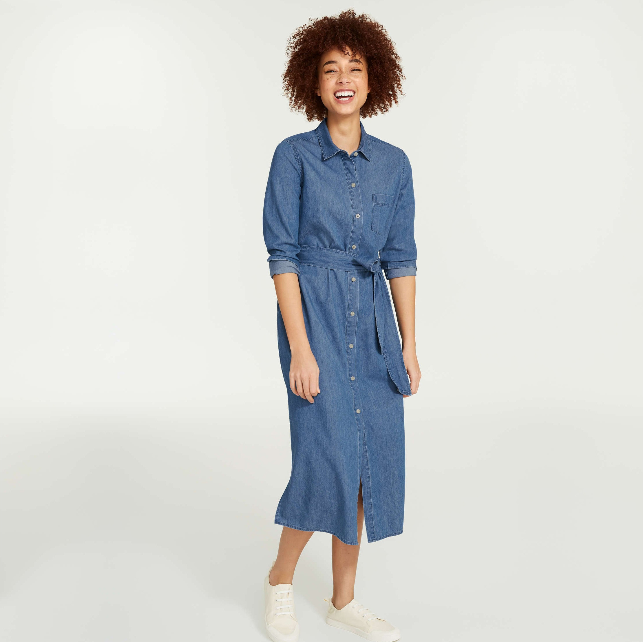 A person wearing a long denim shirtdress with rolled up sleeves