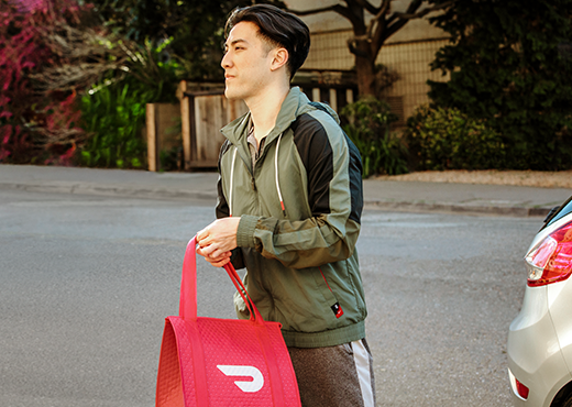 A man walks away from his car holding a DoorDash delivery. 