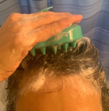 A person rubbing the scalp massager on their soapy head of hair 