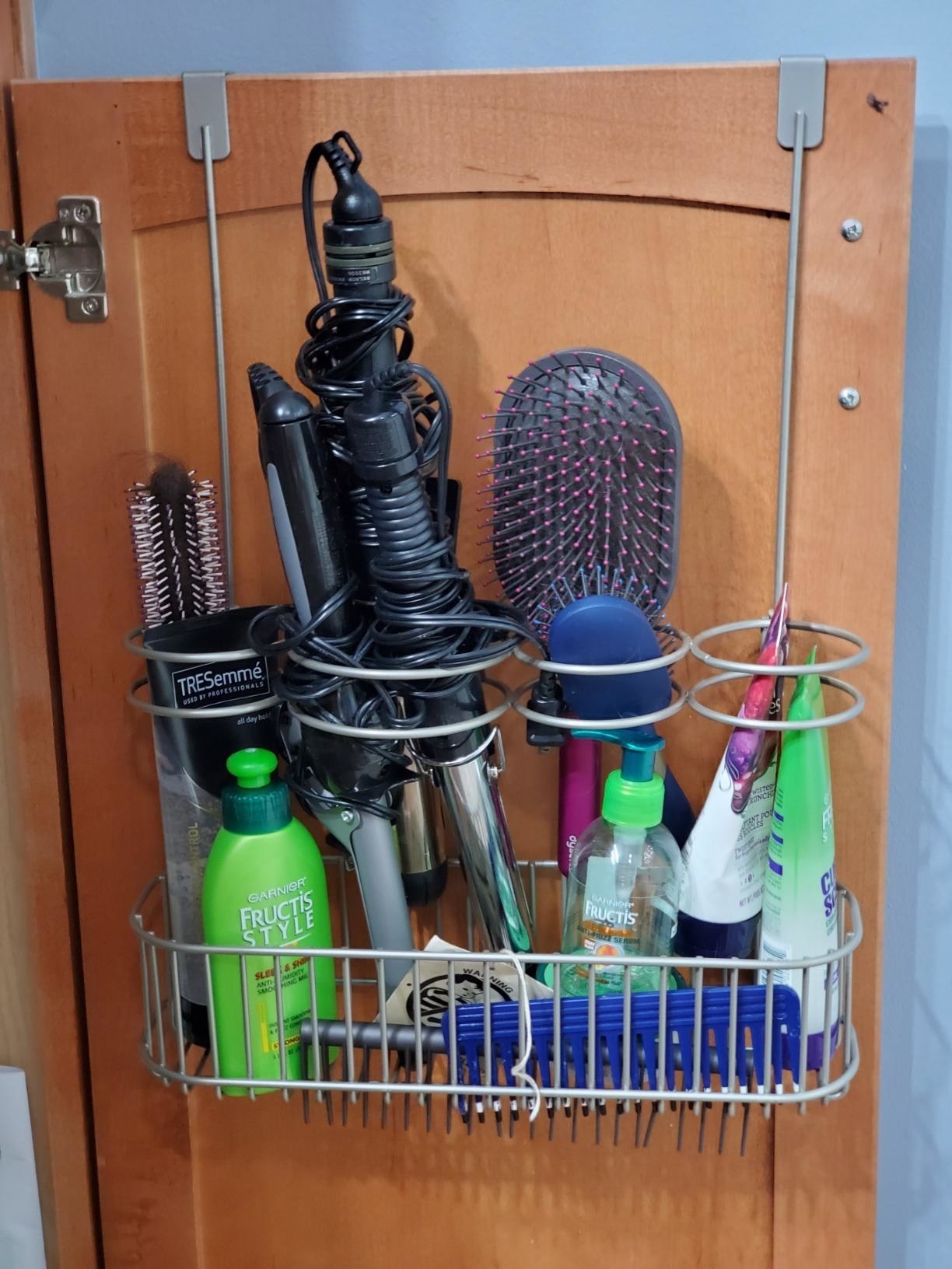 reviewer image of the mDesign over door hair care organizer hanging on the inside of a bathroom cabinet
