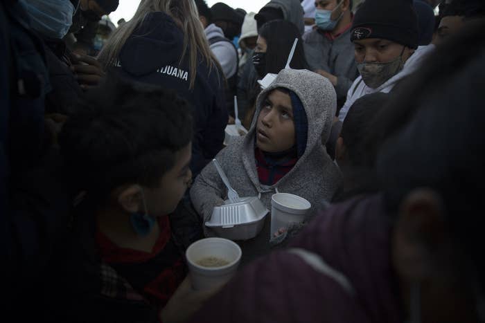 A child wearing a hood and holding a styrofoam food container and cup is surrounded by people