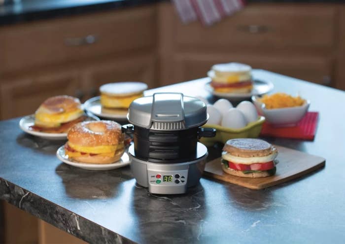 The sandwich maker on a table surrounded by breakfast sandwiches