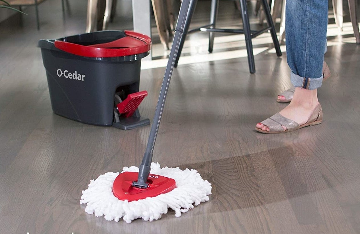 A model uses the red, gray, and white mop with the red and gray spin bucket in the background