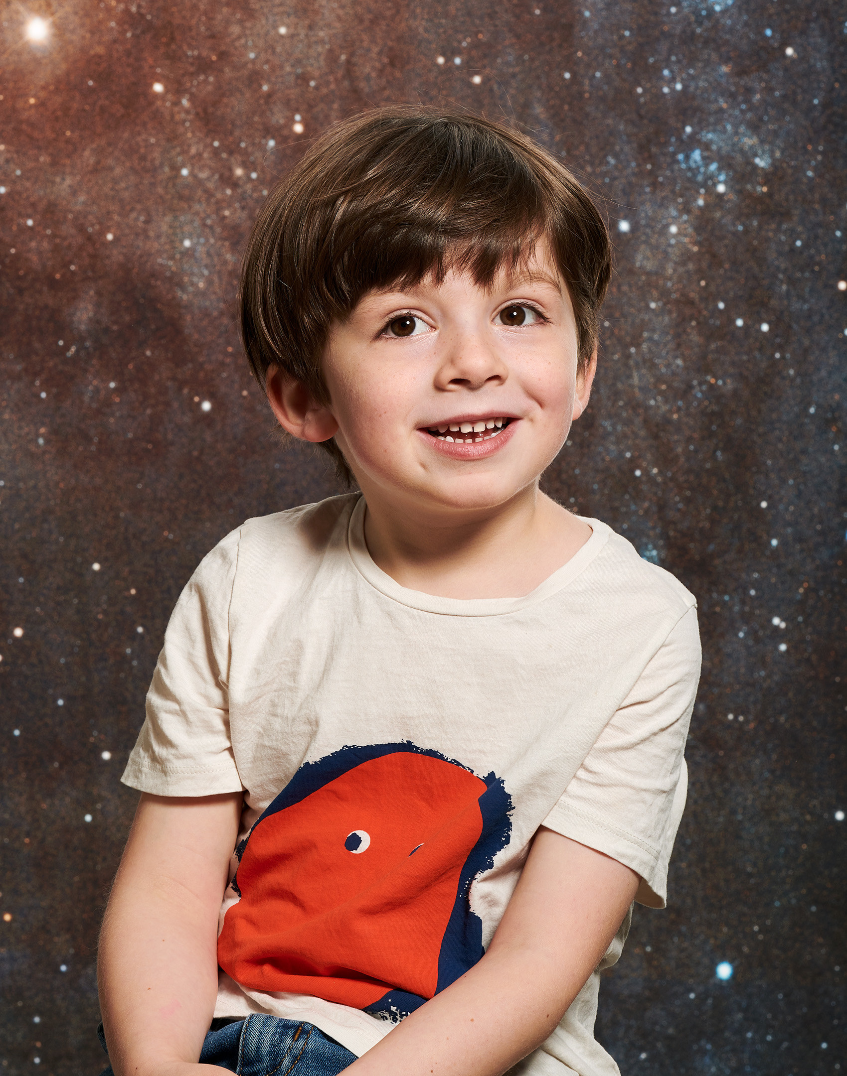 A young boy poses for a portrait in front of a backdrop of a galaxy and stars
