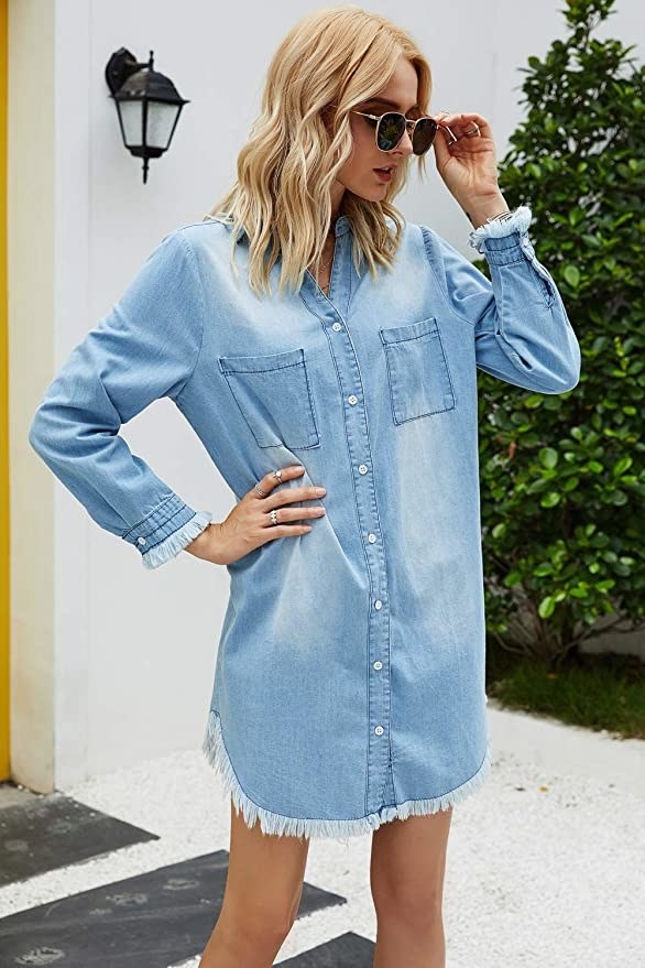 A model wearing the long-sleeved mini dress with frayed cuffs in light wash denim