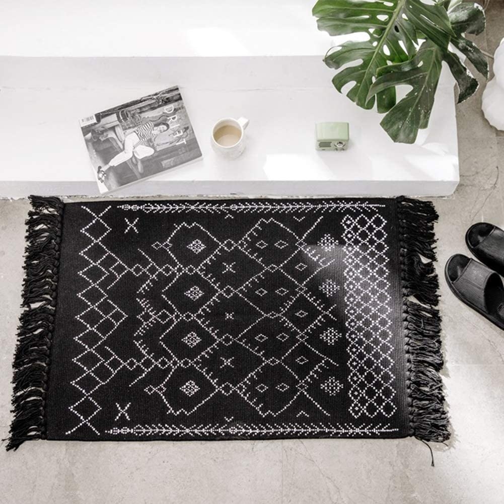 Black rug with tassels on either end and embroidered white geometric patterns 