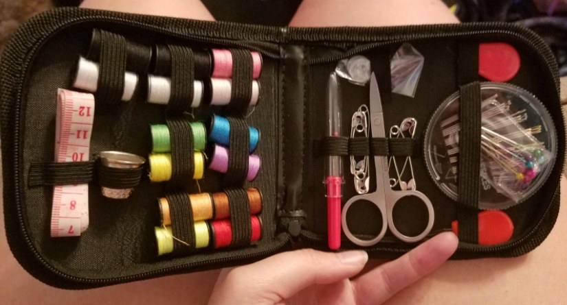 Open black sewing kit with a variety of colors of thread, scissors, and other sewing supplies. 