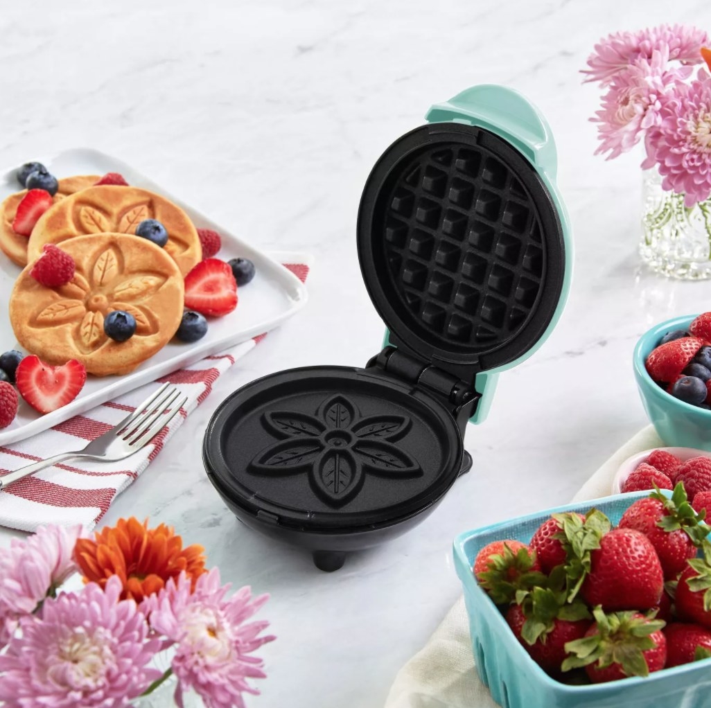 The waffle maker next to a pile of flower printed pancakes 