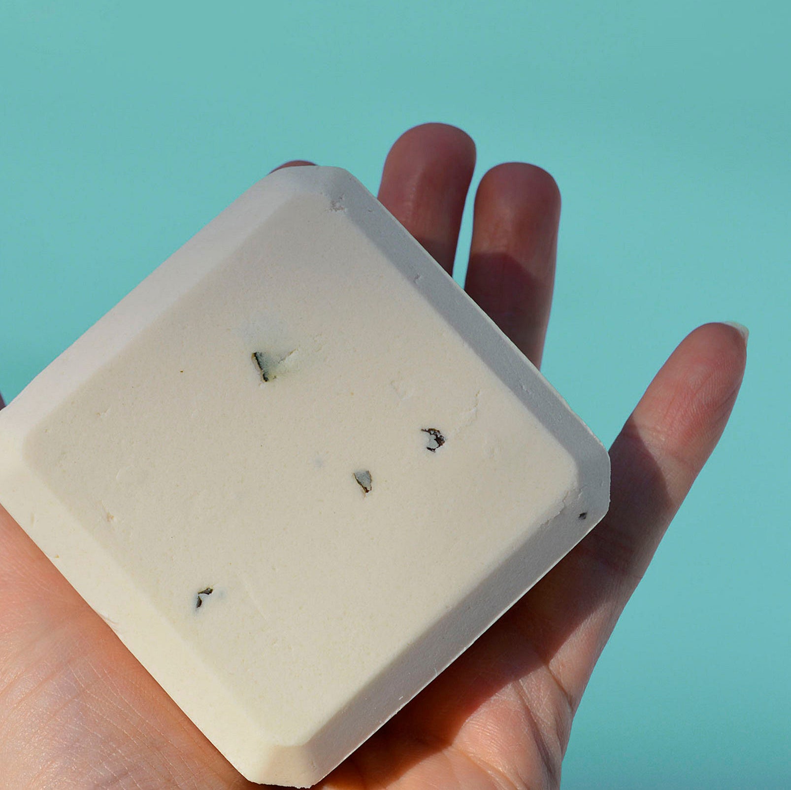 A person&#x27;s hand with a square bar of shampoo 