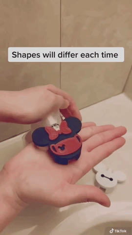 Person pressing on Minnie shaped soap dispenser attachment on nozzle to make suds in the shape of Mickey Mouse 